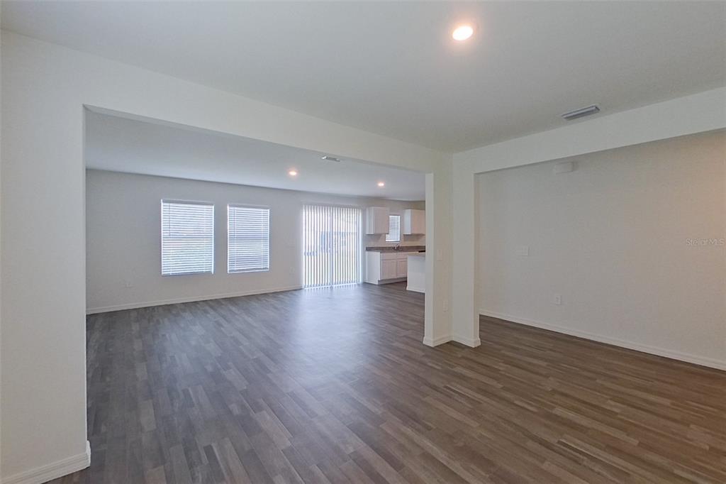 An open-concept living area features wood-look flooring, white walls, and a view into the kitchen — 4020 GARDEN BOULEVARD, CAPE CORAL, FL