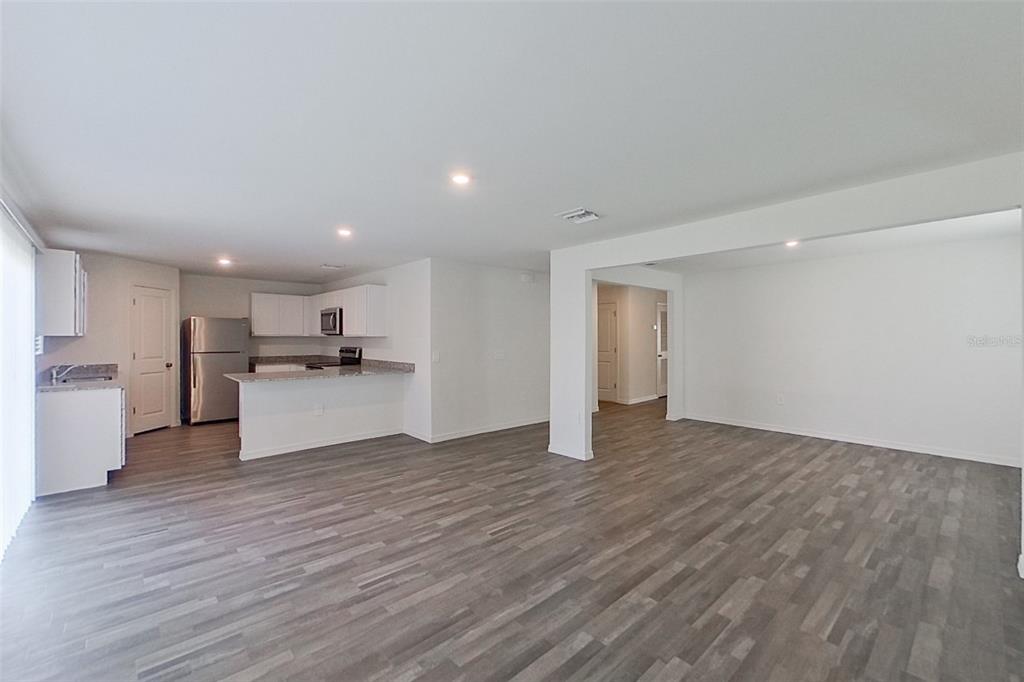 An open-concept living area features gray wood-look flooring, white walls, and a modern kitchen — 4020 GARDEN BOULEVARD, CAPE CORAL, FL
