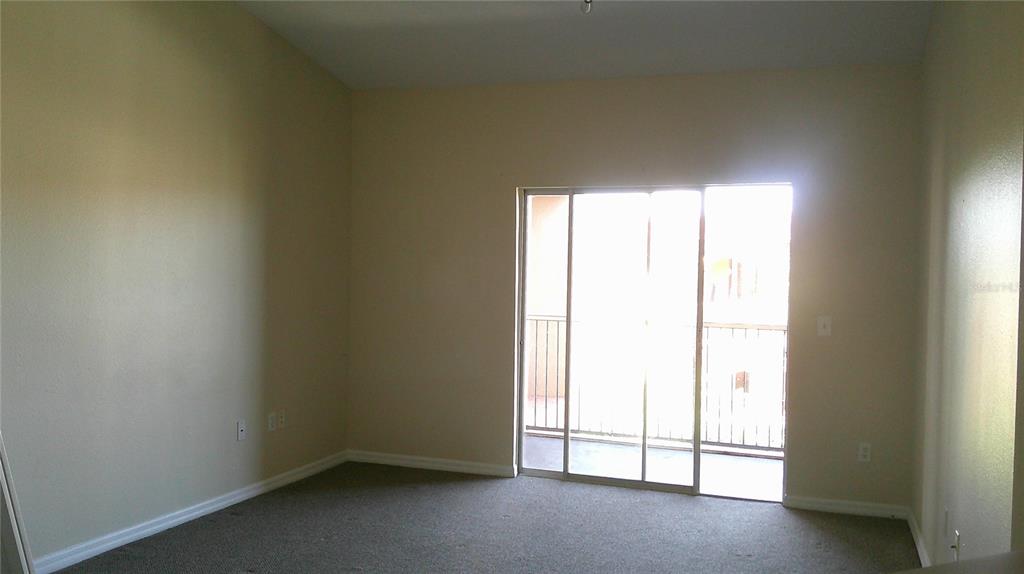 An empty bedroom features beige walls, carpeted flooring, and a sliding glass door to a balcony — 5500 METROWEST BOULEVARD UNIT 304, ORLANDO, FL