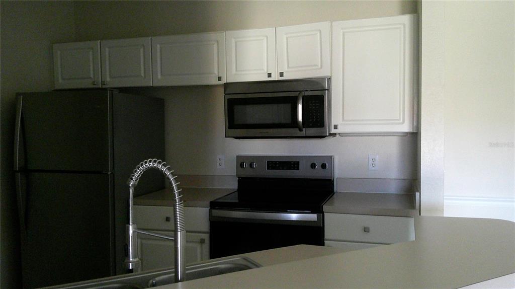 A kitchen features white cabinets, stainless steel appliances, and a curved countertop — 5500 METROWEST BOULEVARD UNIT 304, ORLANDO, FL