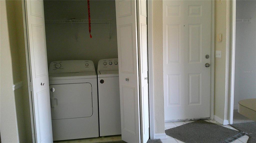 A laundry closet with a washer and dryer sits next to a white entry door — 5500 METROWEST BOULEVARD UNIT 304, ORLANDO, FL