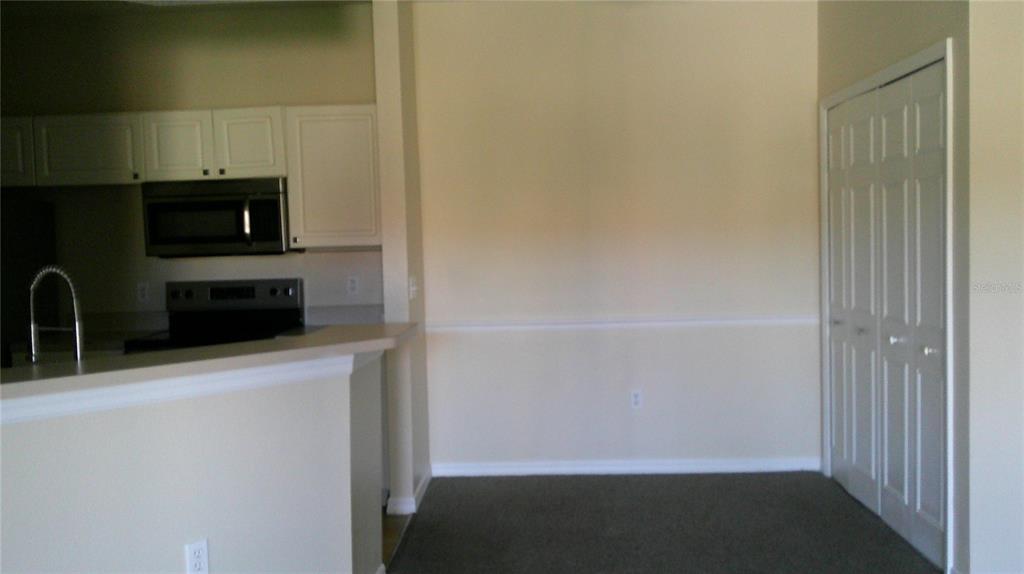 A kitchen with white cabinets and stainless steel appliances opens to a carpeted dining area — 5500 METROWEST BOULEVARD UNIT 304, ORLANDO, FL