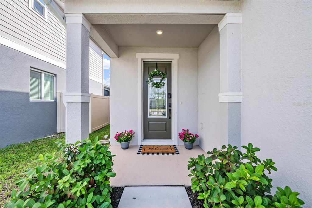 A front porch features a dark door with a wreath, potted flowers, and a welcome mat — 37668 YUKON DRIVE, ZEPHYRHILLS, FL