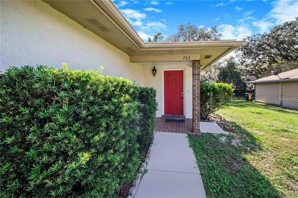 A red front door is centered under a covered porch with a concrete walkway — 733 MIKASUKI DRIVE, LAKELAND, FL