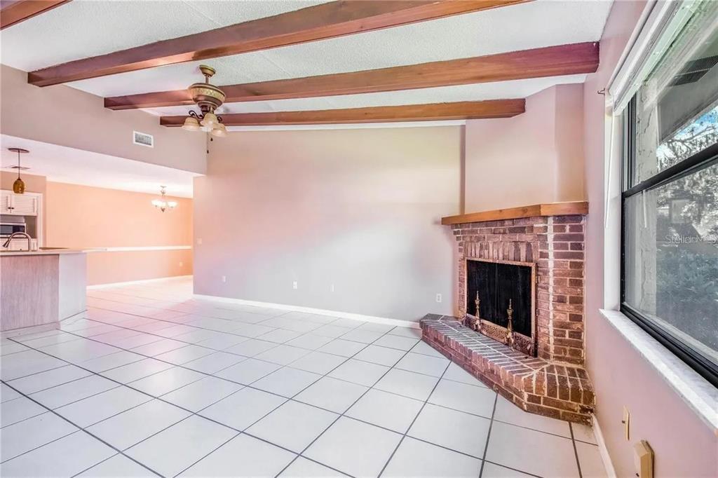 A living room with white tile floors, exposed wood ceiling beams, and a brick fireplace — 733 MIKASUKI DRIVE, LAKELAND, FL