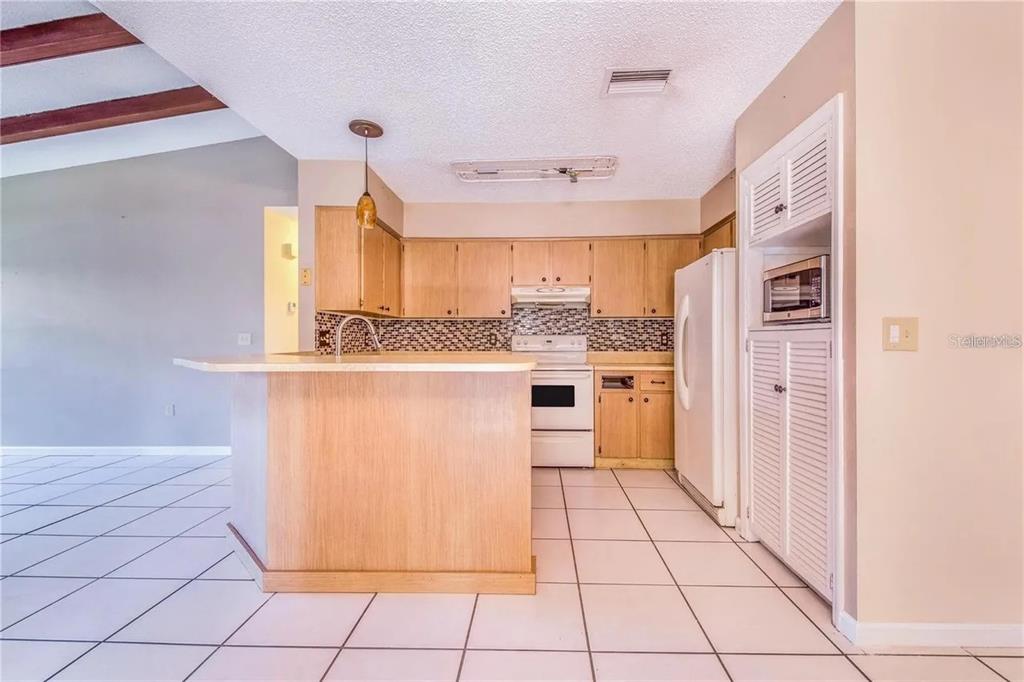 A kitchen features light wood cabinets, white appliances, a breakfast bar, and tiled flooring — 733 MIKASUKI DRIVE, LAKELAND, FL