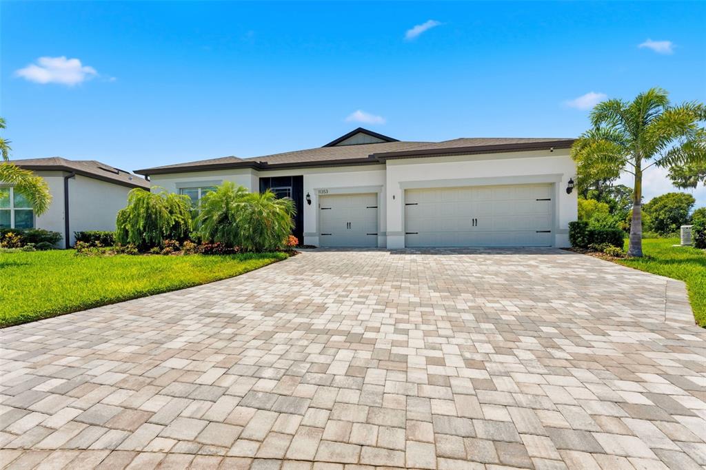 A single-story house with a paved driveway, two garage doors, and palm trees — 11353 OUTRIGGER PLACE, PARRISH, FL