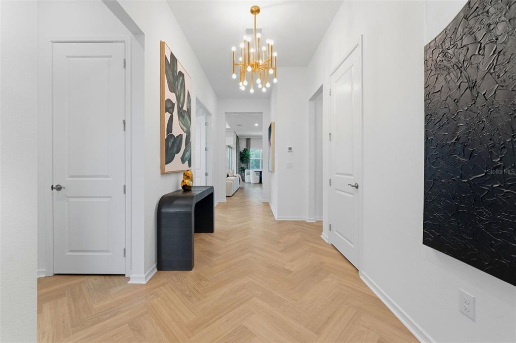 A bright hallway features light wood herringbone floors, a gold chandelier, and white paneled doors — 11353 OUTRIGGER PLACE, PARRISH, FL