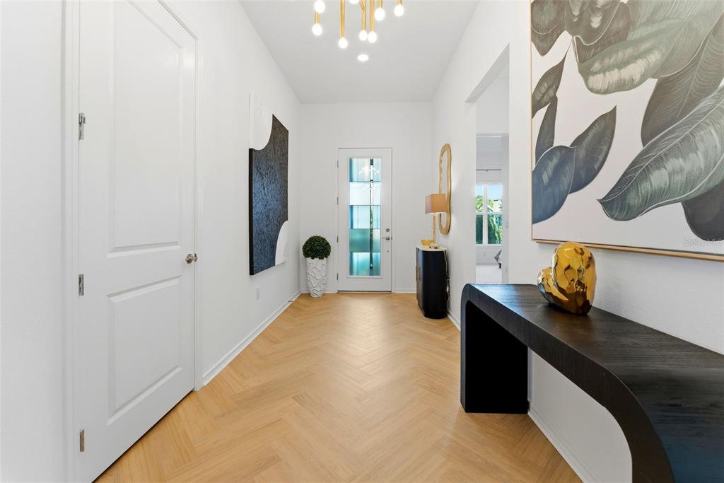 A bright entryway features light wood herringbone floors, a modern chandelier, and a front door — 11353 OUTRIGGER PLACE, PARRISH, FL