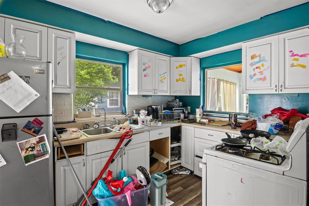 A cluttered kitchen features white cabinets, teal walls, a stainless steel refrigerator, and a stove — 1022 W MARJORIE STREET, LAKELAND, FL