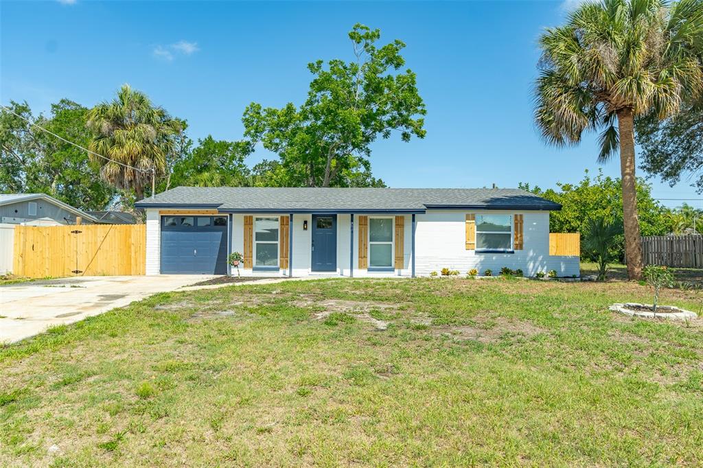 A single-story white house with a blue garage door and front door sits on a lawn — 6304 FLORIDA CIRCLE W, APOLLO BEACH, FL