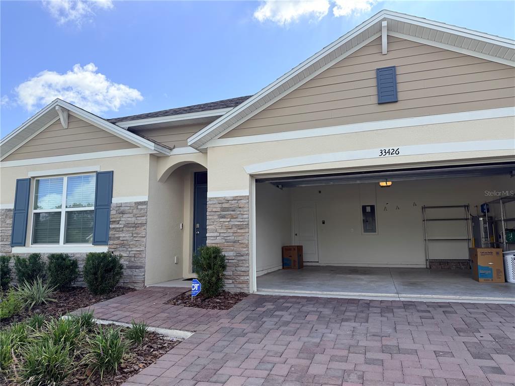 A single-story house exterior features tan siding, stone accents, blue shutters, and a paved driveway — 33426 AFFIRMED WAY, SORRENTO, FL