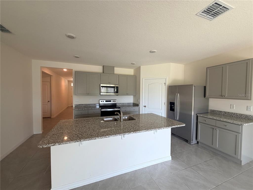 A kitchen features gray cabinets, granite countertops, a central island, and stainless steel appliances — 33426 AFFIRMED WAY, SORRENTO, FL