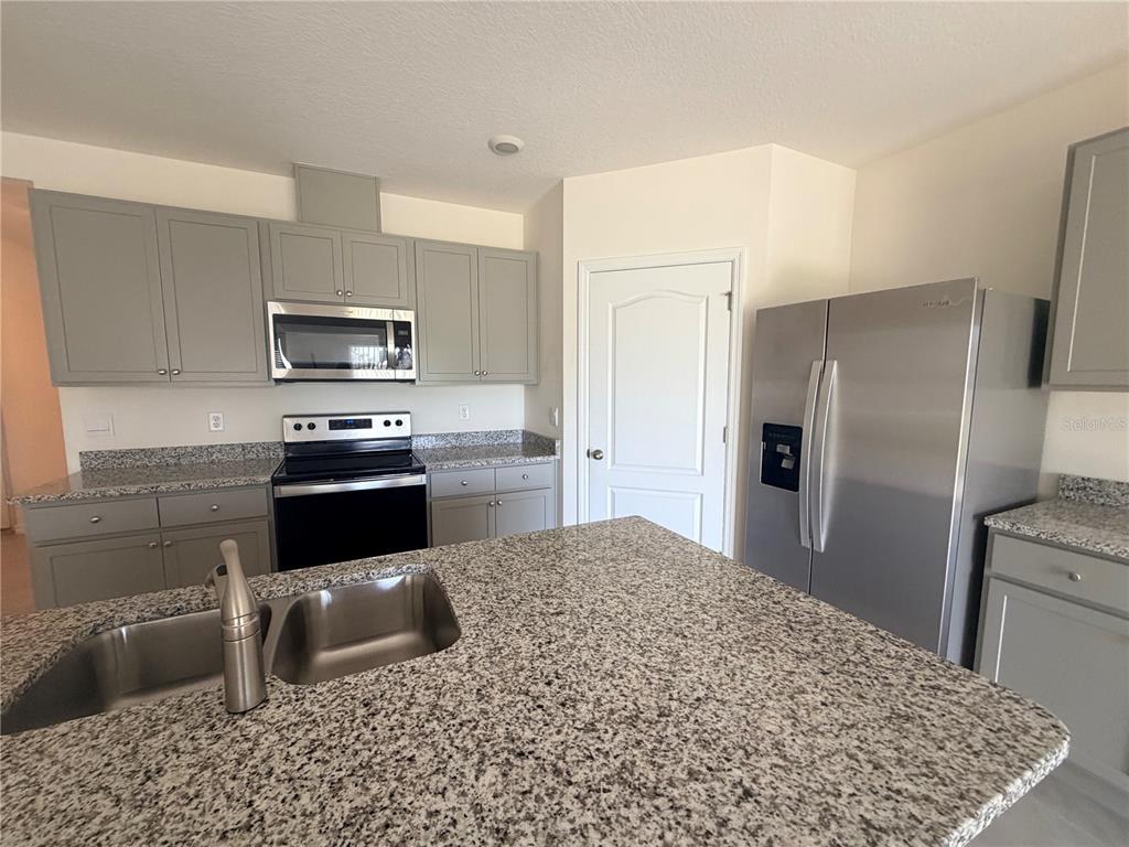 A kitchen features gray cabinets, granite countertops, stainless steel appliances, and a central island — 33426 AFFIRMED WAY, SORRENTO, FL