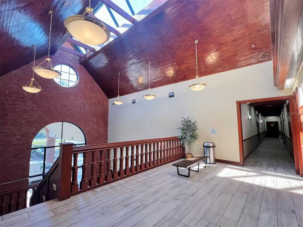 A high-ceilinged hallway features wood-paneled ceilings, a brick wall, a wooden railing, and tile flooring — 2500 W LAKE MARY BOULEVARD UNIT 213, LAKE MARY, FL