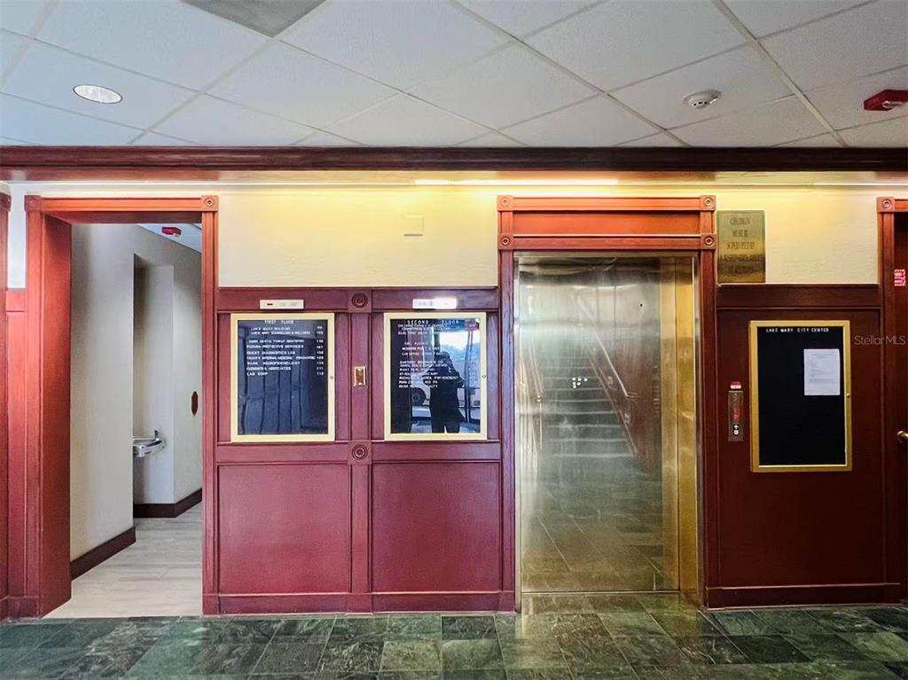 An office building lobby features a stainless steel elevator, directory signs, and dark wood trim — 2500 W LAKE MARY BOULEVARD UNIT 213, LAKE MARY, FL