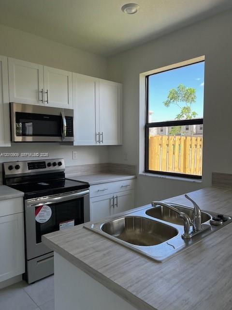 A kitchen with white cabinets, stainless steel appliances, and a double-basin sink by a window — 13102 SW 232nd Ln # 13102, Miami FL 33032, MIAMI, FL