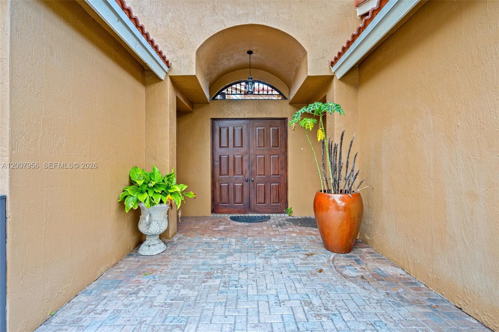 A covered entryway features a brick floor, double wooden doors, and two large potted plants — 16403 Diamond Head Dr, Weston FL 33331, WESTON, FL