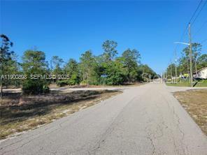 A paved road leads toward a vacant, wooded lot at a street intersection — 1600 E 15TH STREET, LEHIGH ACRES, FL