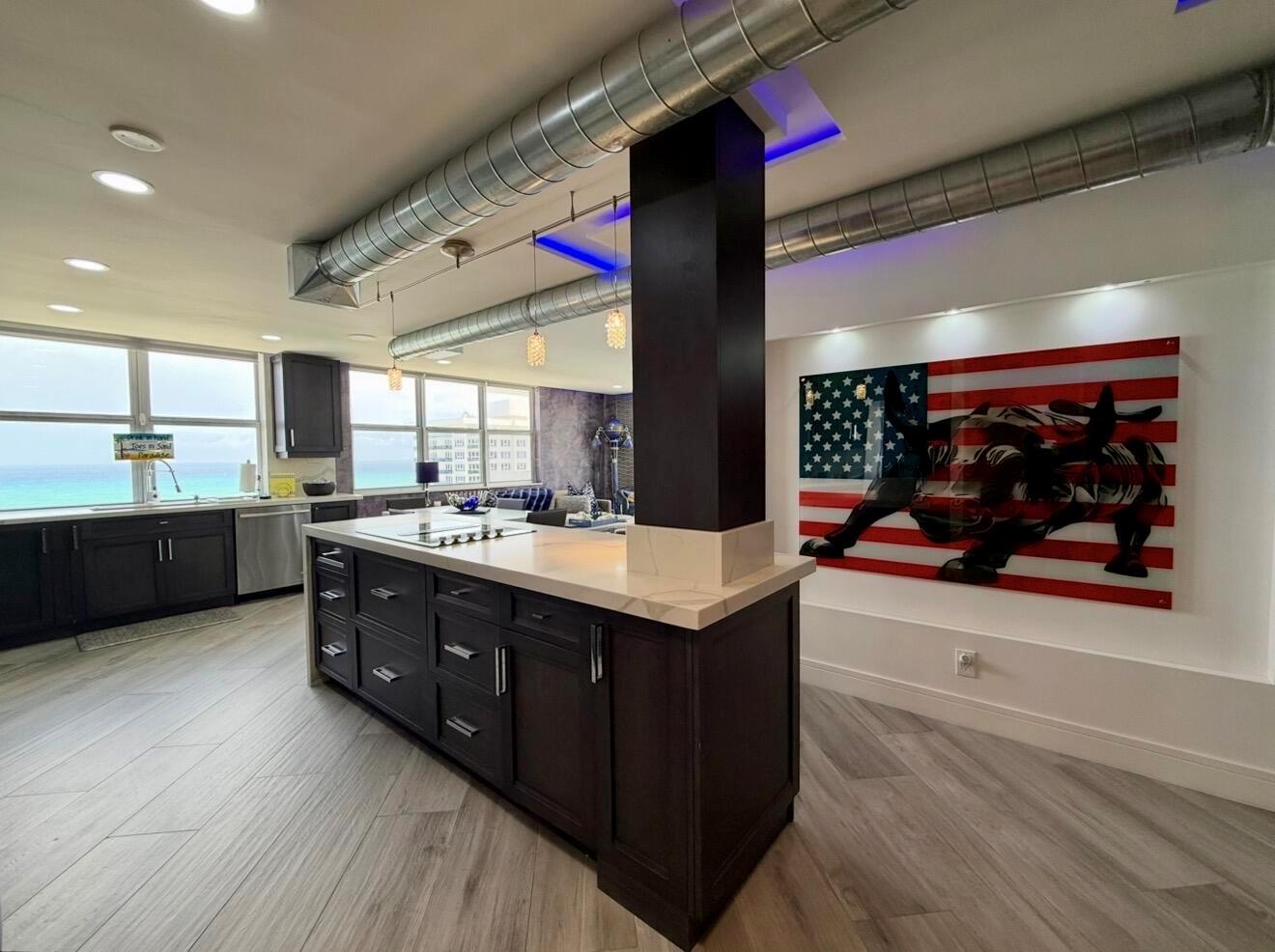 A modern kitchen features a dark wood island, exposed ductwork, and a large bull-themed artwork — 2121 N Ocean Boulevard # 1409e, Boca Raton FL 33431, BOCA RATON, FL