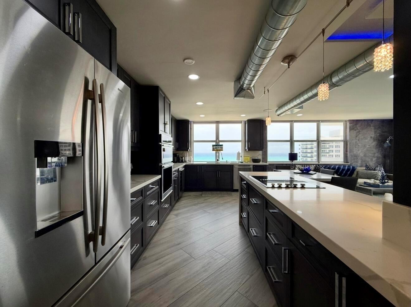 A modern kitchen with dark cabinetry, stainless steel appliances, and an island overlooking the ocean — 2121 N Ocean Boulevard # 1409e, Boca Raton FL 33431, BOCA RATON, FL