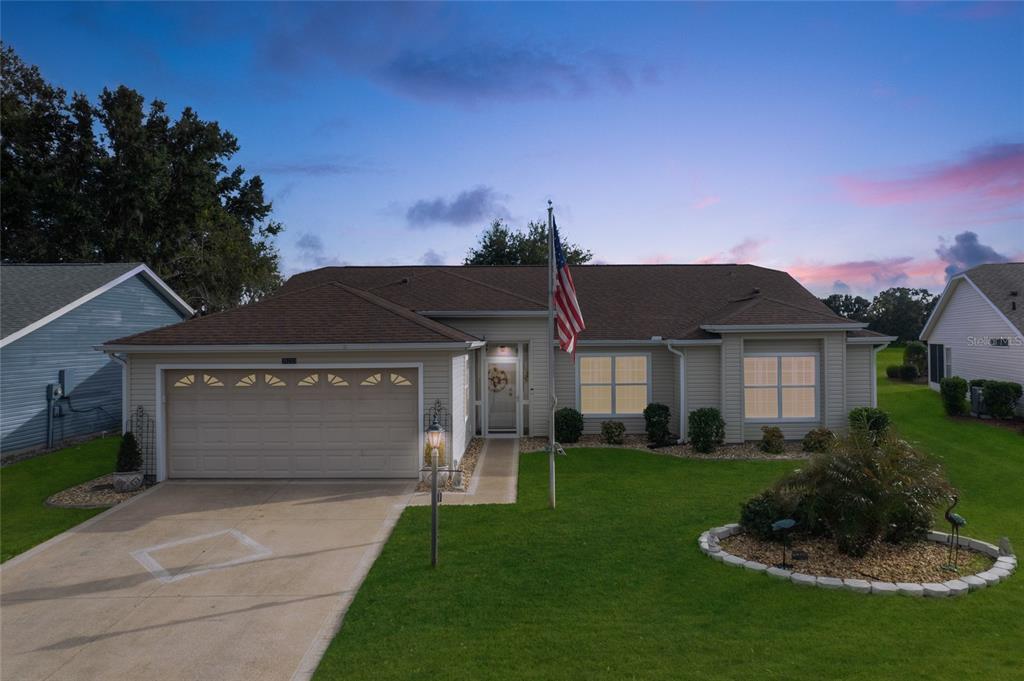 A single-story house with beige siding, a two-car garage, and an American flag in front — 25233 LOST OAK CIRCLE, LEESBURG, FL