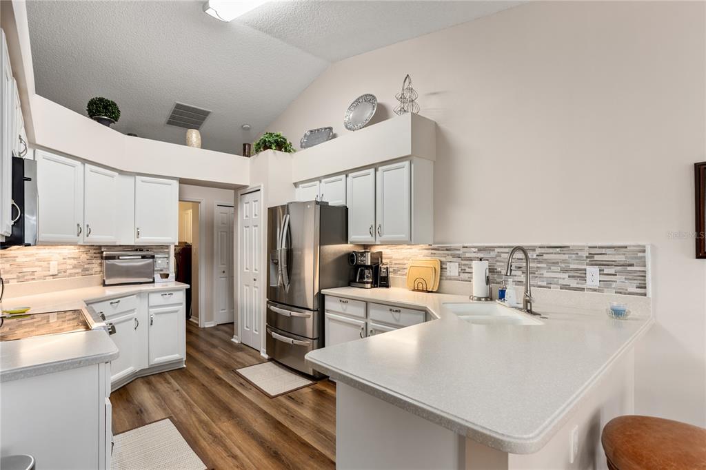 A kitchen with white cabinets, stainless steel appliances, a tiled backsplash, and wood-look flooring — 25233 LOST OAK CIRCLE, LEESBURG, FL