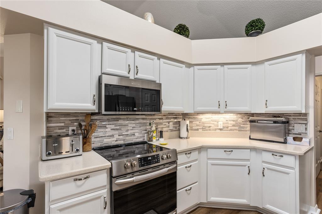 A kitchen features white cabinets, stainless steel appliances, and a multi-toned glass tile backsplash — 25233 LOST OAK CIRCLE, LEESBURG, FL