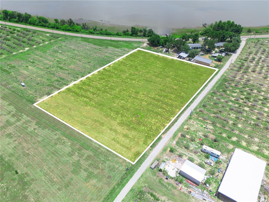 An aerial view shows a rectangular, grass-covered vacant lot bordered by a road and nearby buildings — 0 FLOOD ROAD, FROSTPROOF, FL