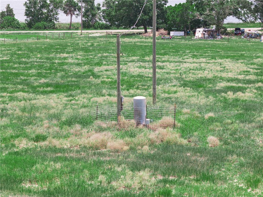 An open grassy field features a utility pole and a fenced-in well pump — 0 FLOOD ROAD, FROSTPROOF, FL