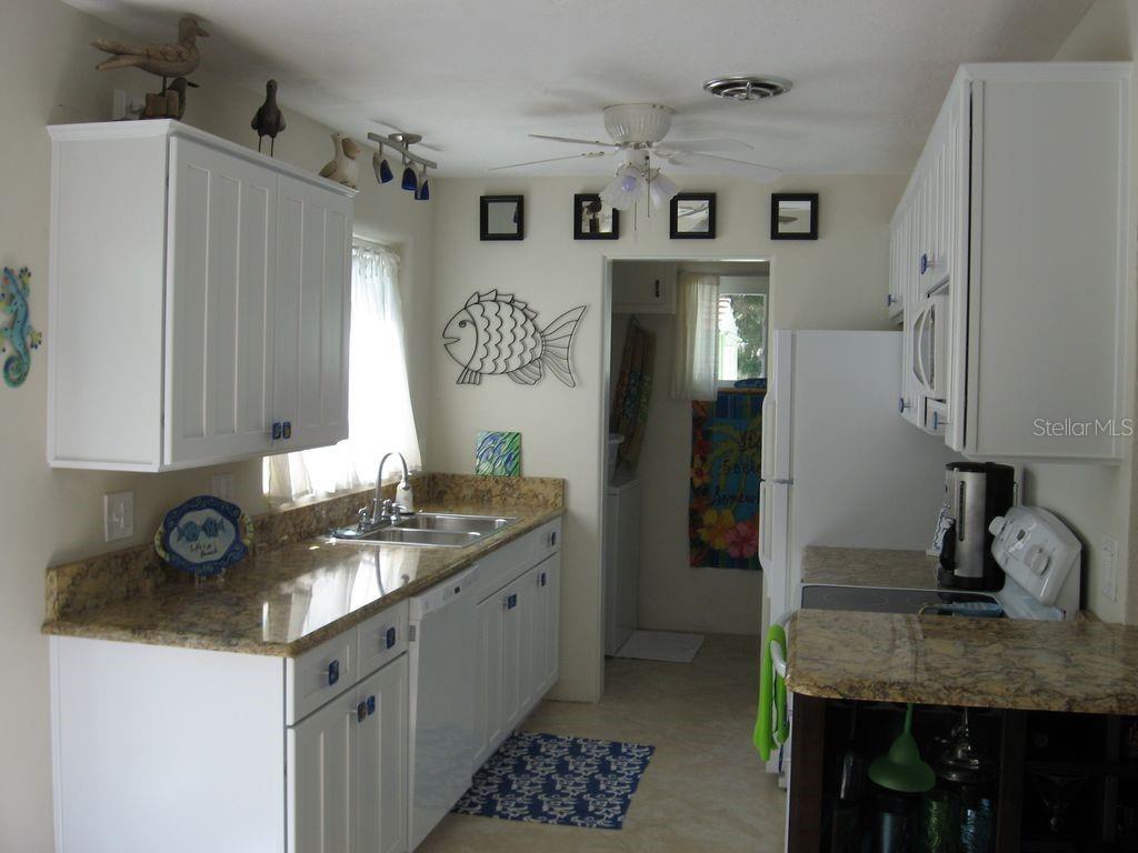 A kitchen with white cabinets, granite countertops, a double sink, and coastal-themed wall decor — 411 S Pine STREET, NEW SMYRNA BEACH, FL