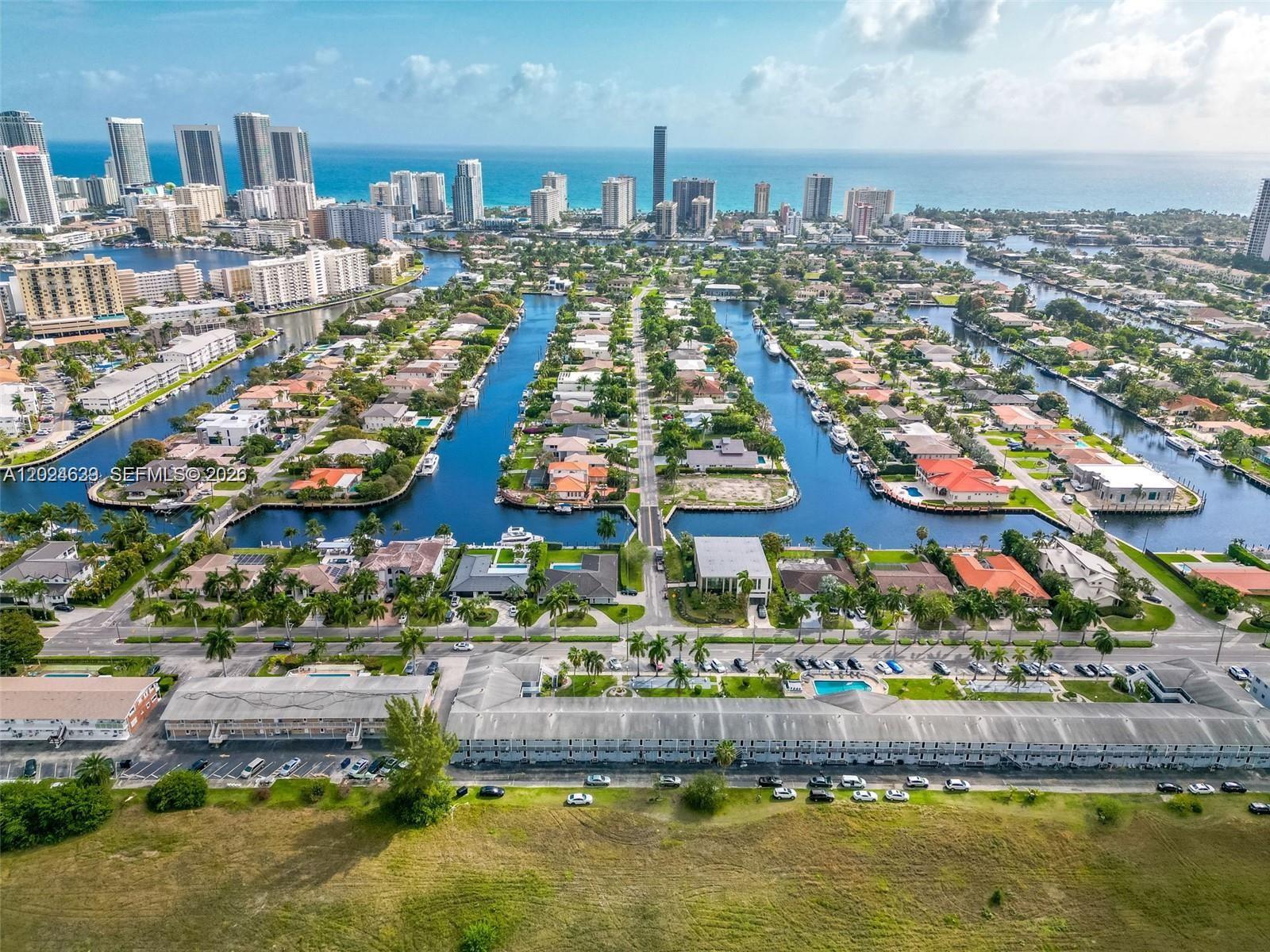 An aerial view shows a residential neighborhood with canals, houses, and high-rise buildings nearby — 600 Layne Blvd # 212, Hallandale Beach FL 33009, HALLANDALE BEACH, FL