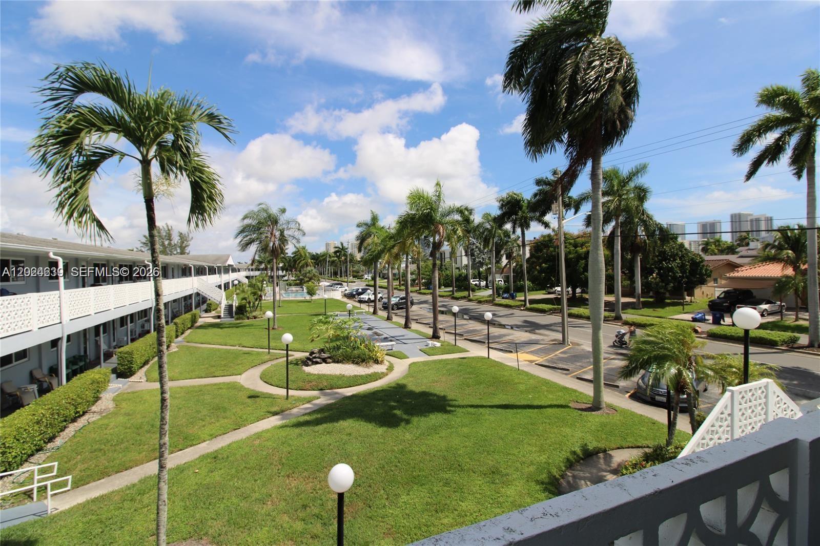 An elevated view shows a grassy courtyard with palm trees, walkways, and a parking lot — 600 Layne Blvd # 212, Hallandale Beach FL 33009, HALLANDALE BEACH, FL