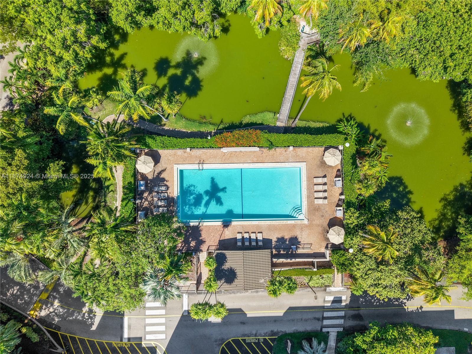 An aerial view shows a rectangular swimming pool surrounded by a patio, trees, and ponds — 101 Crandon Blvd # 381, Key Biscayne FL 33149, KEY BISCAYNE, FL