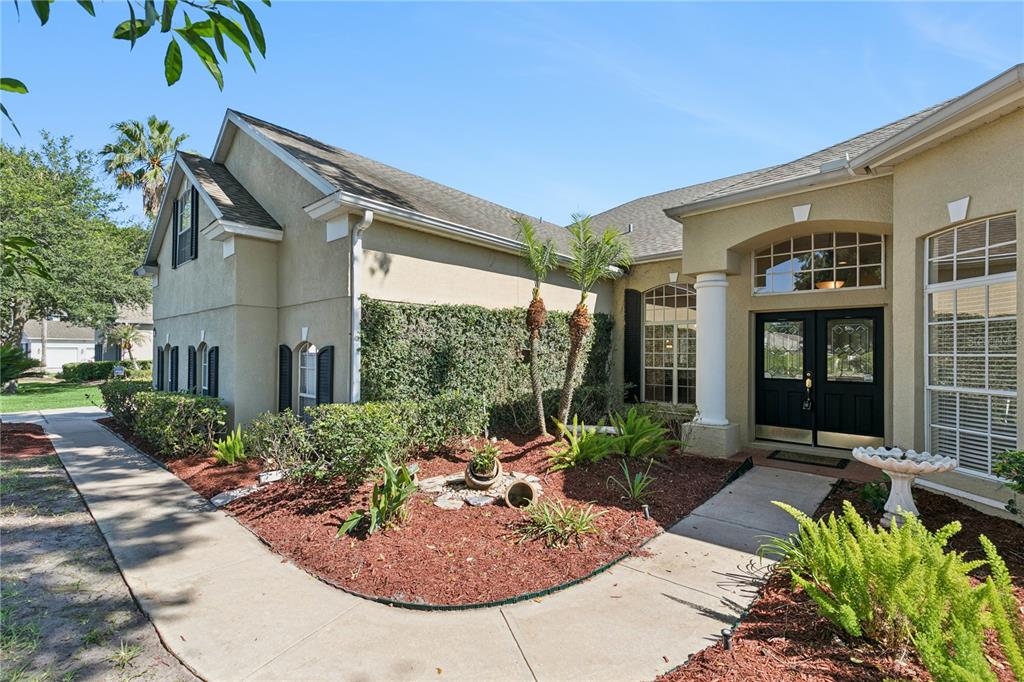The exterior of a tan house features a front entrance, landscaping, and a concrete walkway — 5700 CLIMBING ROSE WAY, SANFORD, FL