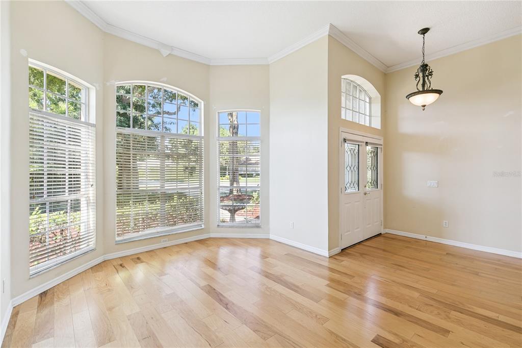 A bright, empty room features wood-look flooring, large windows, and a white double-door entrance — 5700 CLIMBING ROSE WAY, SANFORD, FL