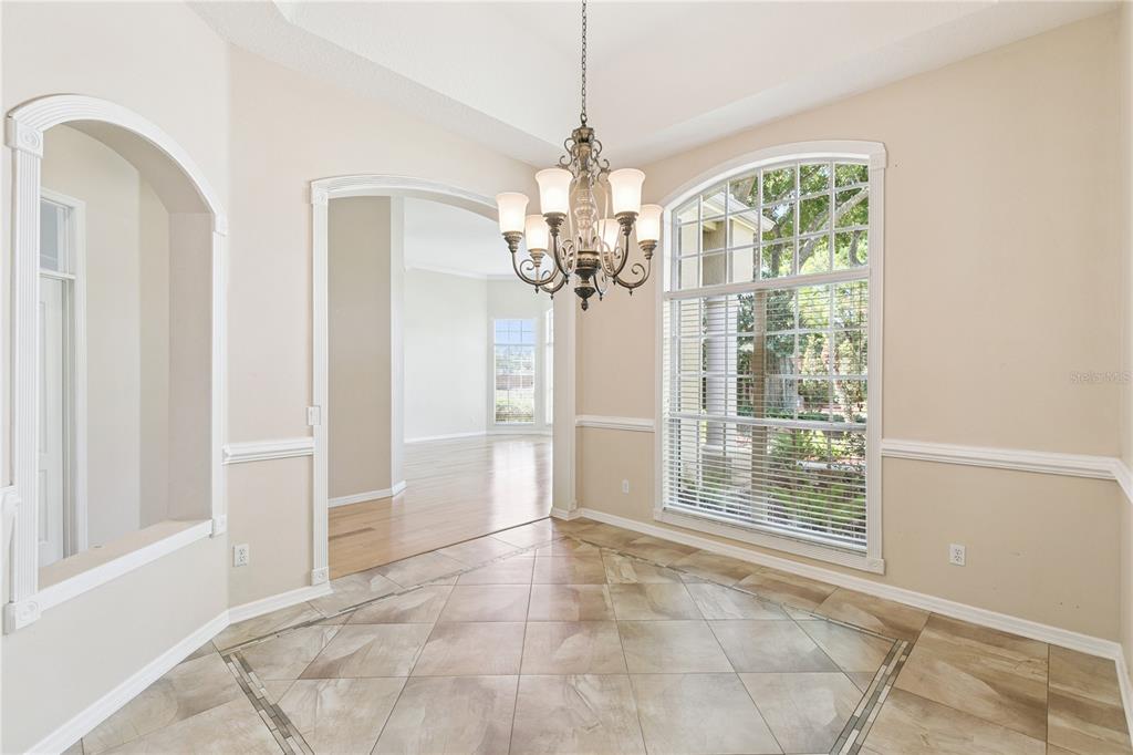 A dining room with tile flooring, a chandelier, and an arched window overlooking trees — 5700 CLIMBING ROSE WAY, SANFORD, FL