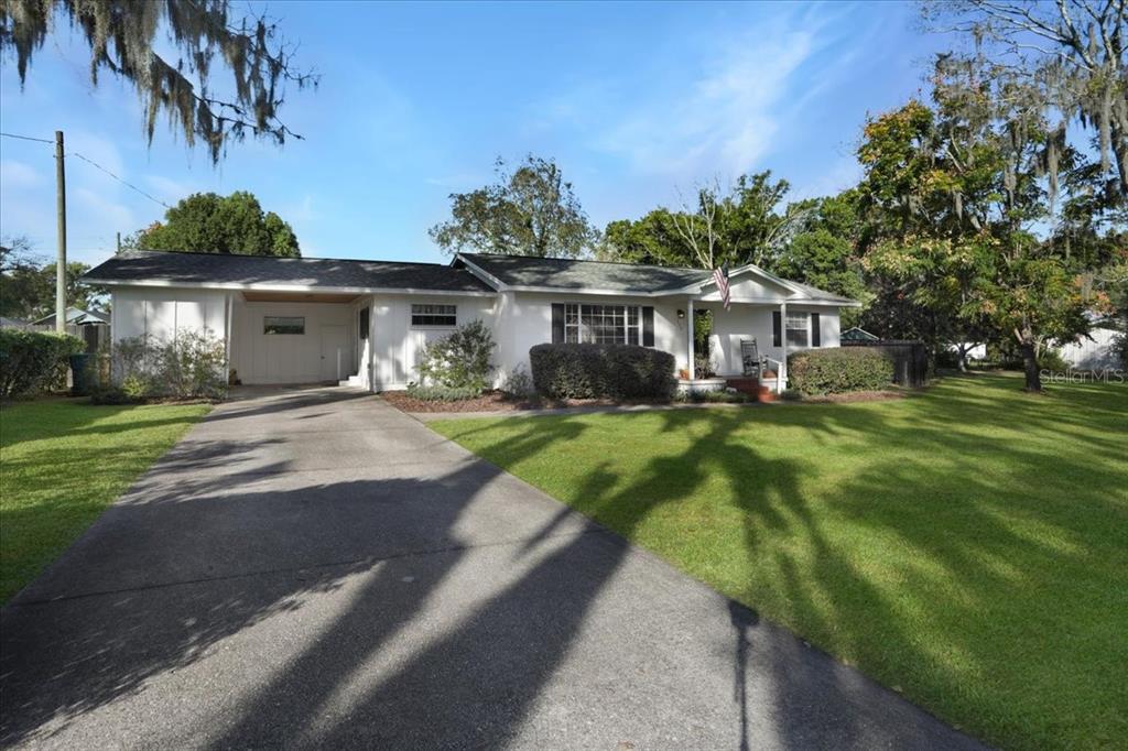 A white single-story house with a carport and a large front lawn under a blue sky — 220 SE 28TH AVENUE, OCALA, FL