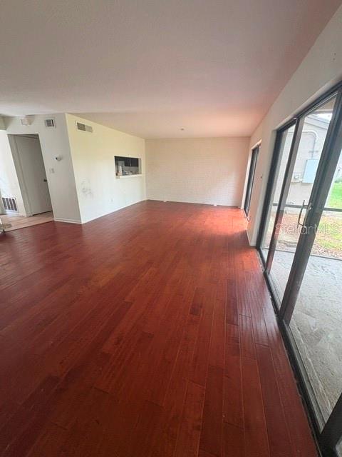 An empty living room features dark wood flooring, white walls, and a large sliding glass door — 459 MEADOWOOD BOULEVARD, FERN PARK, FL