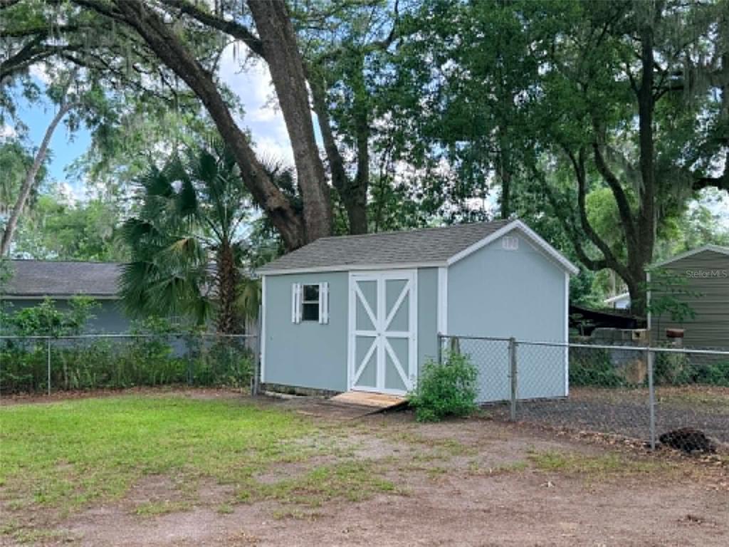 A light blue storage shed with white trim sits in a grassy backyard — 1774 NE 12TH STREET, OCALA, FL