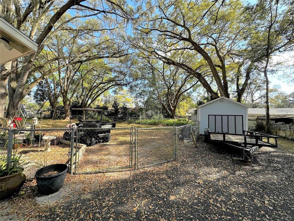 A fenced backyard features a utility shed, a flatbed trailer, and a parked utility vehicle — 1774 NE 12TH STREET, OCALA, FL