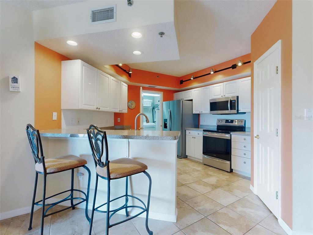 A kitchen features white cabinetry, granite countertops, stainless steel appliances, and orange accent walls — 5300 S ATLANTIC AVENUE UNIT 6-206, NEW SMYRNA BEACH, FL