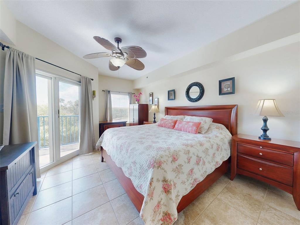 A bedroom features a wooden bed, tile flooring, a ceiling fan, and a sliding glass door — 5300 S ATLANTIC AVENUE UNIT 6-206, NEW SMYRNA BEACH, FL
