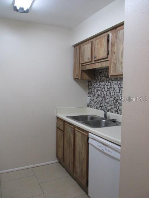 A kitchen features wood cabinets, a mosaic tile backsplash, a double sink, and a dishwasher — 14227 SHADOW MOSS LANE UNIT 102, TAMPA, FL