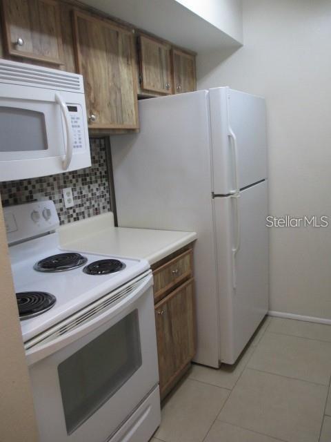 A kitchen features white appliances, wood-toned cabinets, and a mosaic tile backsplash — 14227 SHADOW MOSS LANE UNIT 102, TAMPA, FL