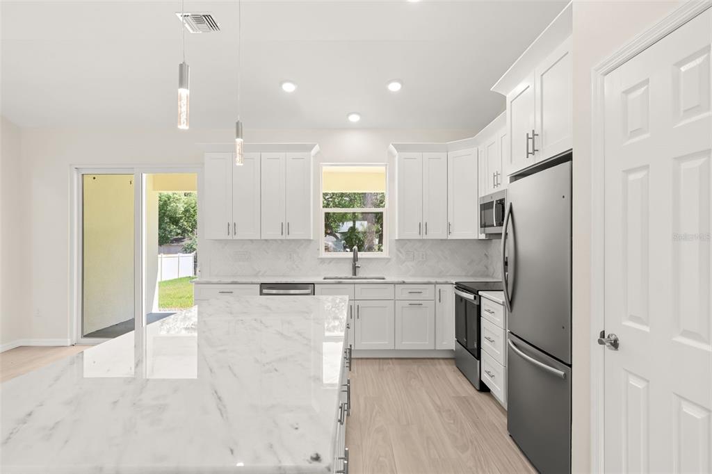 A modern kitchen features white cabinetry, marble-look countertops, stainless steel appliances, and a large island — 247 DEBARY DR, DEBARY, FL
