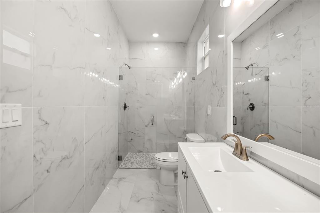 A modern bathroom features white marble-look tile walls, a glass-enclosed shower, and a white vanity — 247 DEBARY DR, DEBARY, FL