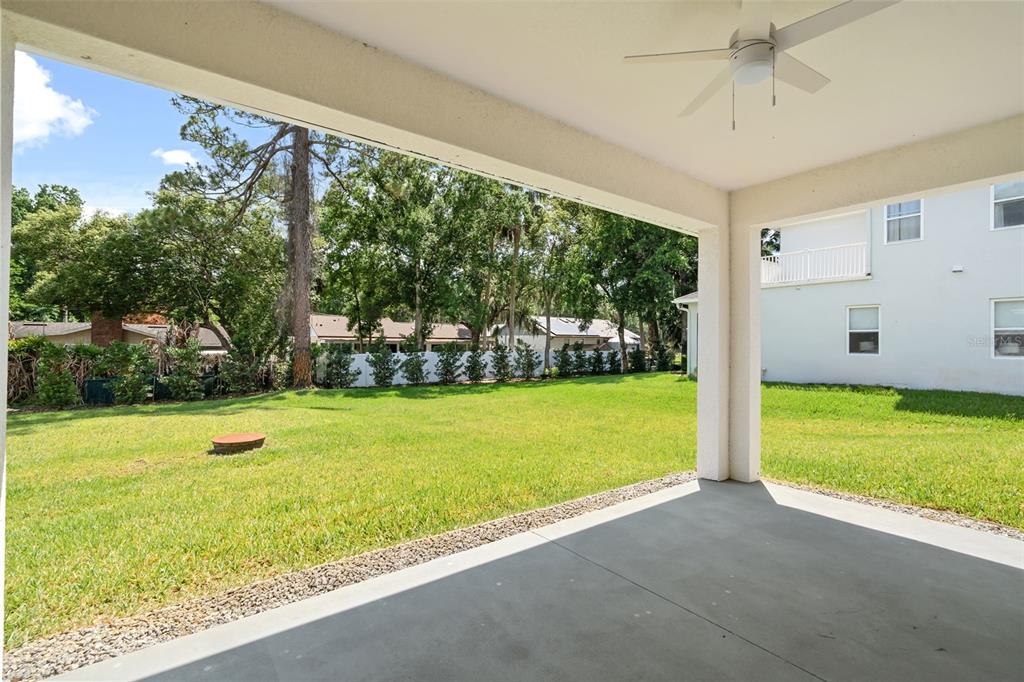 A covered concrete patio overlooks a grassy backyard with trees and a neighboring house — 247 DEBARY DR, DEBARY, FL