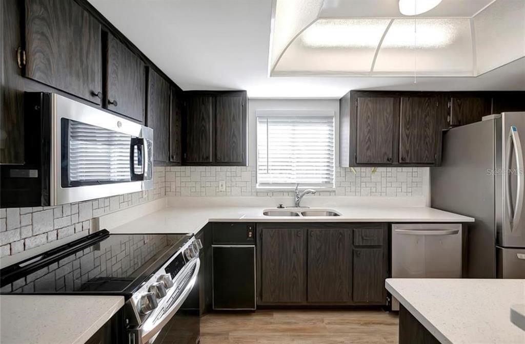 A kitchen features dark wood cabinets, white countertops, stainless steel appliances, and a tiled backsplash — 7020 COGNAC DRIVE UNIT 3, NEW PORT RICHEY, FL
