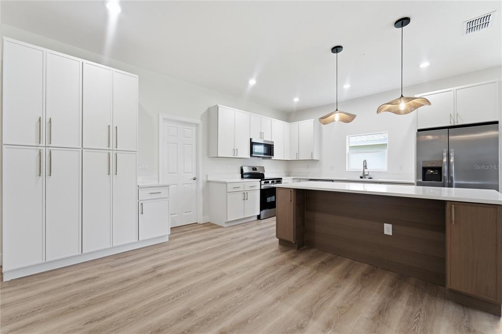 A modern kitchen features white cabinetry, a wood-toned island, stainless steel appliances, and light flooring — 1324 MARSHALL DRIVE, LEESBURG, FL